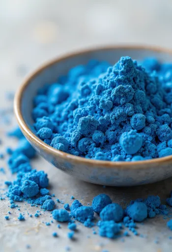 Sinine spirulina pulber väikeses klaasis, erksinine värv, ümbritsetud vetikatega